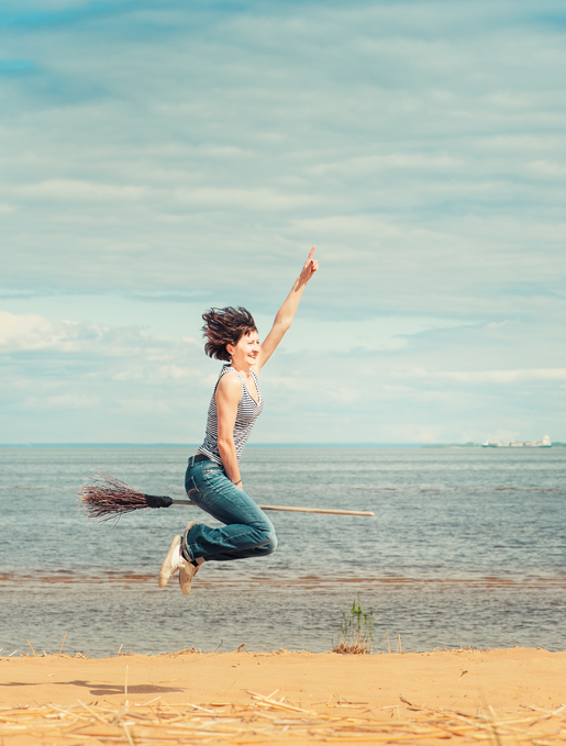 Happy woman with broom jumping on the beach